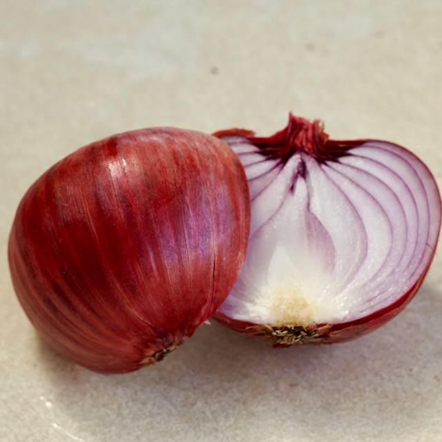 Un oignon Rossa di Milano de Tourne-Sol, coupé en deux, met en valeur ses couches intérieures vives avec une peau extérieure violet foncé et des cercles concentriques blancs/violet clair. Cet oignon exquis repose gracieusement sur une surface légère, incarnant l&#39;art de la nature.