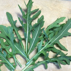 Un bouquet de feuilles de Roquette Sauvage Sylvetta sur une planche à découper de Tourne-Sol.