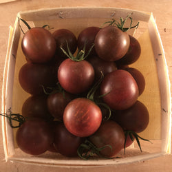Un panier rempli de tomates Tourne-Sol Tomate Cerise Noire sur une table en bois.
